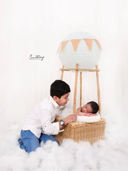 Including siblings in themed shots can be so much fun. Here, a proud big brother looks on as his new baby sister rests in the hot air balloon basket, creating a sweet story of shared adventure.