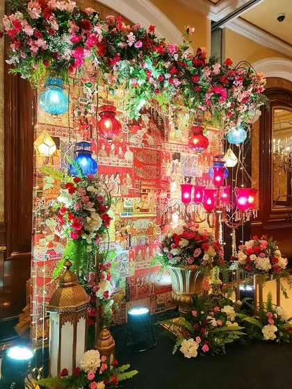 A vibrant and colorful photo corner for the Sufi Night. The backdrop features traditional Indian textile art, decorated with hanging lanterns and lush floral arrangements.