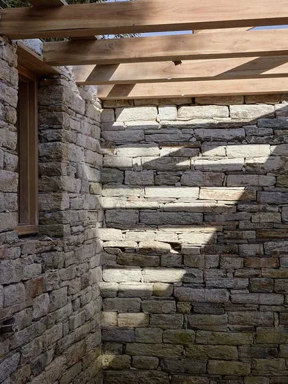 Sunlight casts strong shadows across a newly built stone wall, highlighting the texture and rhythm of the masonry. The interplay of light and stone is a key consideration in our design process.