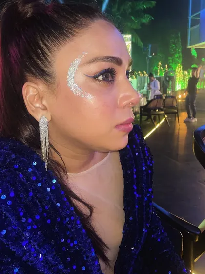 A classic festival look featuring a silver glitter crescent. This design beautifully complements the client's makeup and sequined jacket, perfect for a night of music and dancing.