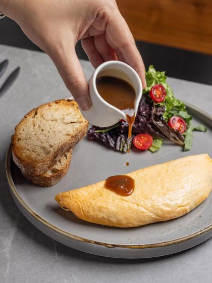 A pour of red wine lamb jus completes the Braised Lamb Omelette, adding another layer of savory depth.