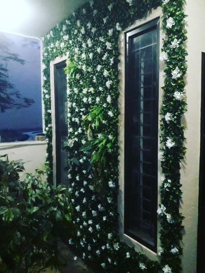 An elegant exterior wall covered in artificial greenery and white flowers. I can install these panels around windows and architectural features to blend them into the design.