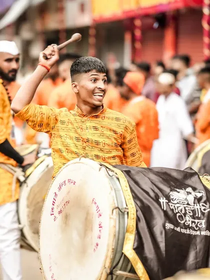 A dhol player with a wide smile, his stick raised, captured in a moment of pure joy and energy.