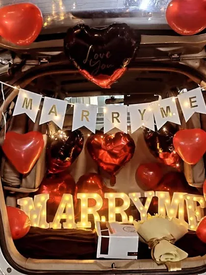 A unique and creative car boot proposal setup. We arranged "MARRY ME" marquee letters, heart-shaped balloons, and fairy lights inside the car's trunk for a surprise proposal she won't forget.