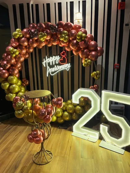 A 25th anniversary celebration with a balloon ring in chrome colors. The large marquee numbers and a 'Happy Anniversary' neon sign make for a stylish photo corner.