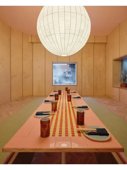 A private dining room at Lucky Chan, featuring a long table with a custom tile runner. The space is enclosed with wood paneling and illuminated by a large, handmade raw silk lamp, creating a warm and intimate setting.