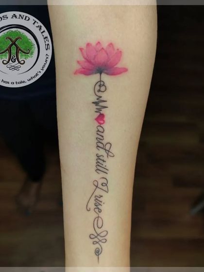 A custom script tattoo that reads "And still I rise," integrated with a lotus, heartbeat, and Unalome symbol. This is a popular and empowering design we customized for the client.