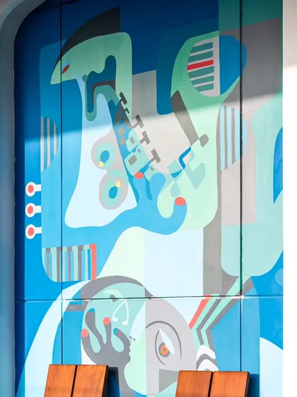 A close-up of the 'Embrace' mural, where shadows from the sun create an ever-changing interplay with the painted forms, adding a dynamic quality to the outdoor art piece.