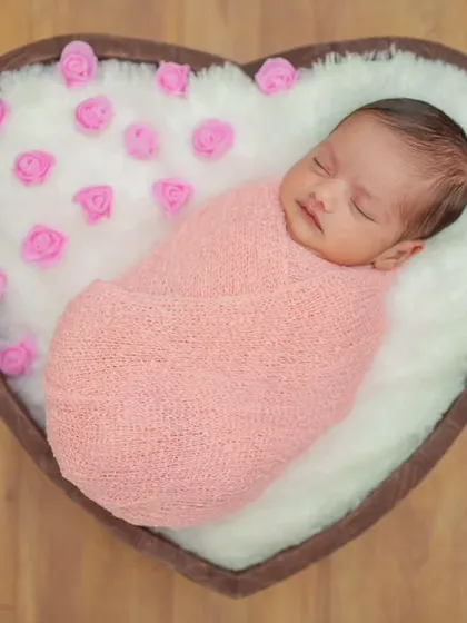 A beautifully composed shot of a newborn nestled in a heart-shaped basket. The pink roses complement the swaddle, adding a delicate and loving touch to the portrait.