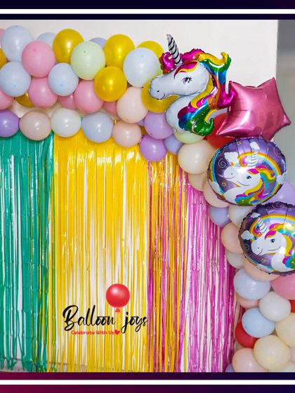 A magical unicorn-themed party backdrop. This setup features a rainbow of pastel balloons, shimmering fringe curtains, and a large unicorn foil balloon to create a whimsical and colorful celebration.