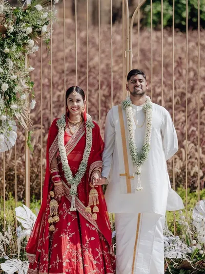 A beautiful shot of the couple during their day wedding ceremony. The backdrop features a modern gold frame decorated with delicate white flowers and pampas grass.