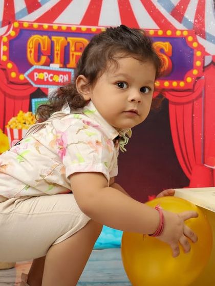 Step right up to the circus. This toddler is exploring the colorful and exciting circus theme, complete with a big top backdrop, popcorn signs, and fun props to play with.