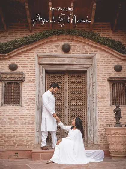 Elegance in simplicity. This serene portrait, with the couple in coordinated white traditional wear, creates a look of pure, understated royalty against a rustic, heritage-style doorway.