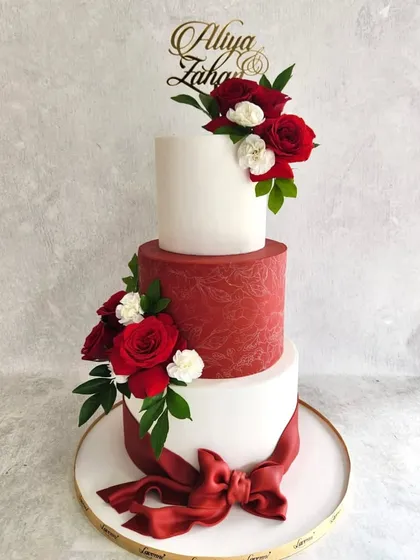 A classic combination of red and white for a wedding is always a winner. This three-tiered cake features a textured crimson tier, a big fondant bow, and is adorned with fresh red and white roses for a romantic finish.