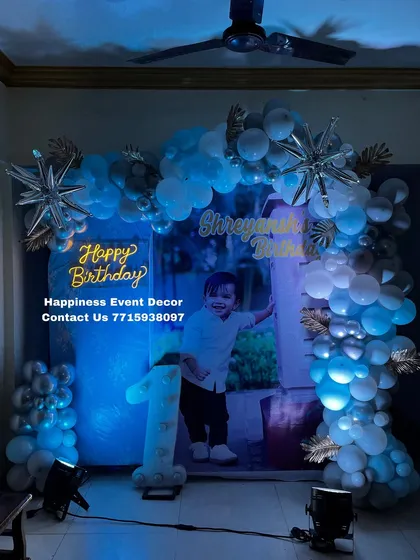 Another angle of the cool-toned blue and silver first birthday home decor. The spotlights highlight the balloon arch and personalized photo backdrop effectively.