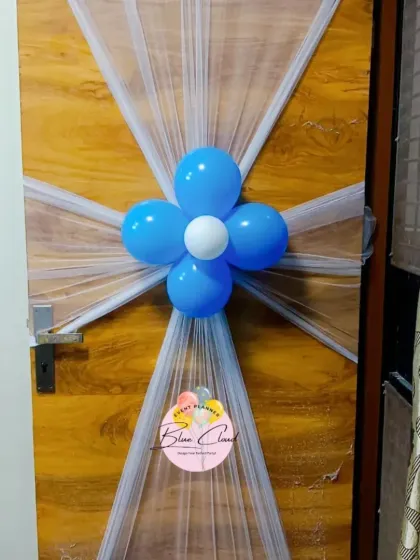 A simple and elegant door decoration using white netting and a blue balloon flower to welcome guests.