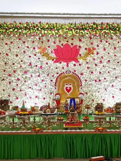 A baby shower setup with a lotus-themed backdrop made of flowers. The plate decoration is arranged neatly on a green turf, creating a serene and beautiful scene.