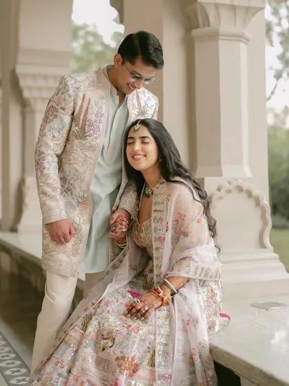 A quiet moment of affection on a palace veranda. The intricate floral outfits of the couple blend beautifully with the regal setting, showcasing a soft, pastel-themed pre-wedding shoot.