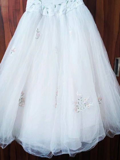 The A-line skirt of the embroidered white gown is made of soft tulle, with matching floral details scattered near the hem.