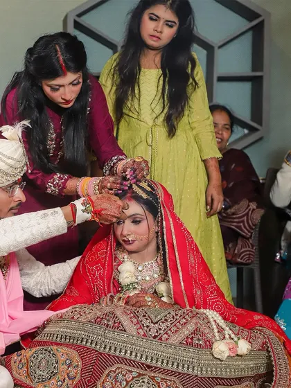 The groom applies sindoor to the bride's forehead, with family members assisting in the ritual. This photo captures the communal and familial nature of Indian weddings, showing the involvement of loved ones in the sacred ceremony.