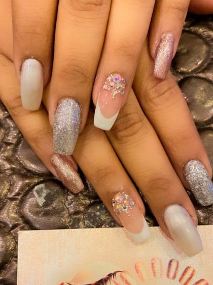 A glamorous set of long, square nails perfect for a bride. The design includes pearly white nails, full-coverage silver glitter nails, and French-tipped nails with crystal clusters.