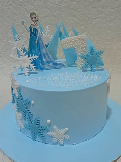 A simple and elegant Frozen theme cake. This light blue cake is decorated with delicate snowflakes and a topper of Queen Elsa, perfect for a winter wonderland party.