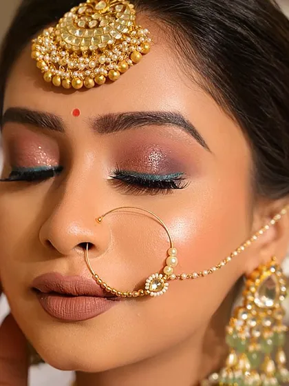 A detailed close-up of a classic bridal eye. This look features a soft, shimmery shadow, a hint of teal liner for a modern touch, and a bold matte lip, perfectly framing the face along with the traditional nath.