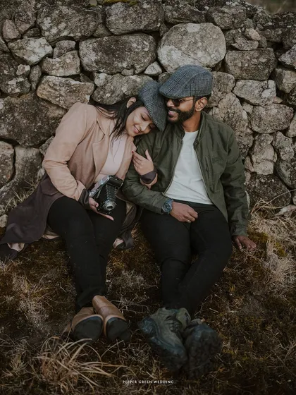 A cozy and romantic moment from a vintage-themed pre-wedding shoot, where the couple rests against a stone wall in the countryside.