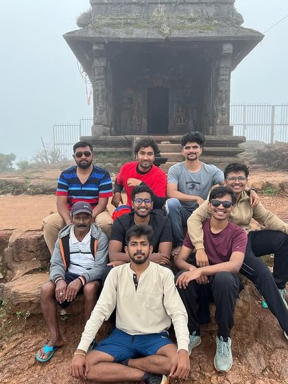 A group rests at a small temple structure on a misty hilltop during the Kodachadri trek.