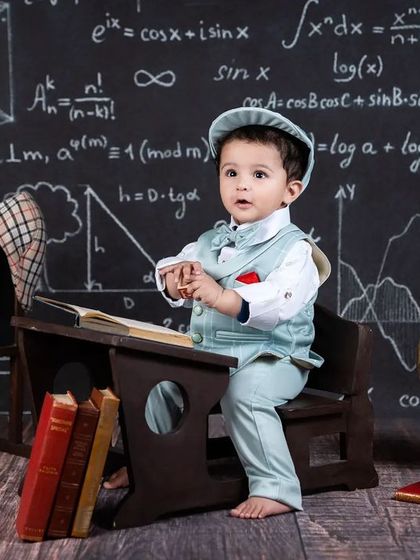 A baby boy sits at his little school desk, looking curious and ready to learn.