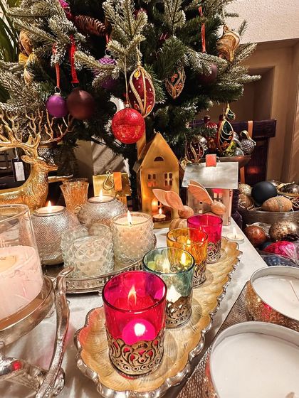 A cozy and festive scene with a variety of my candle holders and votives lighting up a table in front of a Christmas tree.