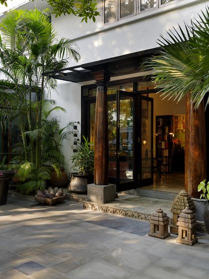The entrance porch of the Courtyard Home, featuring old teakwood columns from Kerala and tribal guardian figures. This space sets a tone of rooted, authentic Indian design from the moment you arrive.