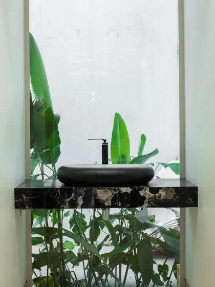 A minimalist powder room where the sink is set against a window overlooking a private green space. This design brings a touch of nature indoors, creating a refreshing and serene experience.
