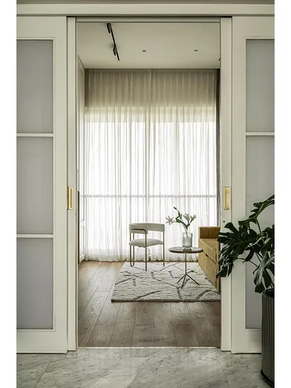 A view into the den room through the sliding pocket doors. The design is both modern and timeless, with warm tones and brass accents creating a luxurious and comfortable atmosphere.