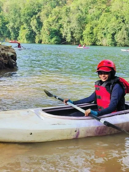 A young girl smiles from her kayak near the riverbank in Dandeli, ready for her next adventure.