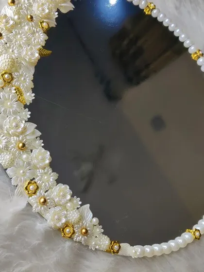 A close-up of the intricate floral and pearl work on the border of the white elegance mirror. Every detail is placed by hand.