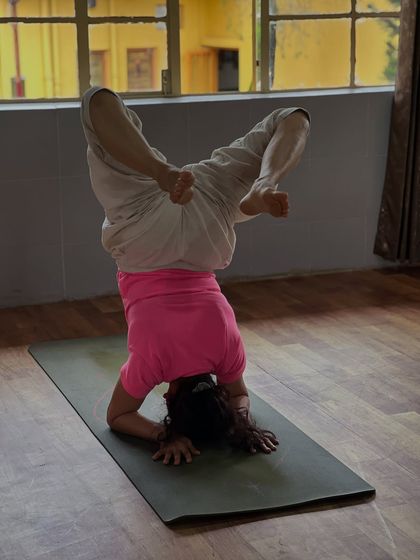 A student practices a variation of Sirsasana, exploring different leg positions to challenge balance and control.