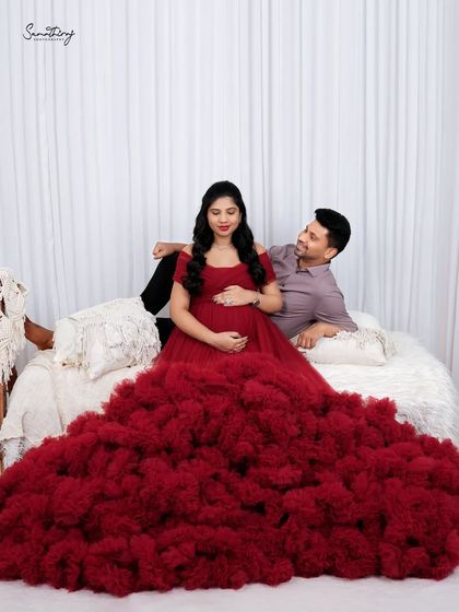 A cozy indoor scene with a couple on a styled bed setup. The vibrant red gown provides a beautiful pop of color against the neutral, boho-inspired decor.