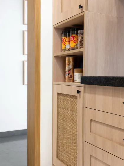 A detail of the pantry cabinet, featuring a wicker mesh door that adds texture and a hint of rustic charm. This thoughtful detail enhances the warm, lived-in feel of the kitchen.