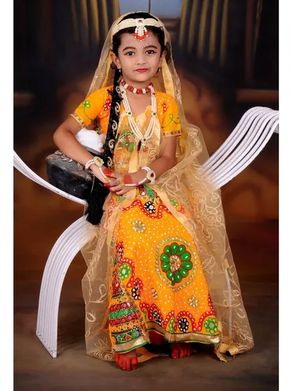 A seated portrait of a young girl in a beautiful Radha costume. I use simple props like this white bench to complement the elaborate traditional attire.