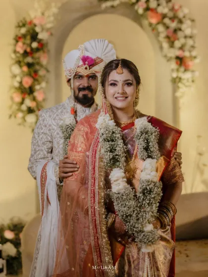 A beautiful couple, their outfits complementing each other in shades of cream and red. Their happy smiles and the lovely floral decor create a warm and inviting wedding portrait.
