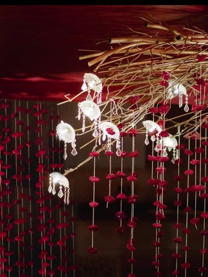 Custom-designed light fixtures featuring delicate glass lamps and crystal droplets hang from golden branches. These elements, combined with red floral strings, created a magical and mesmerizing ambiance over the mandap.
