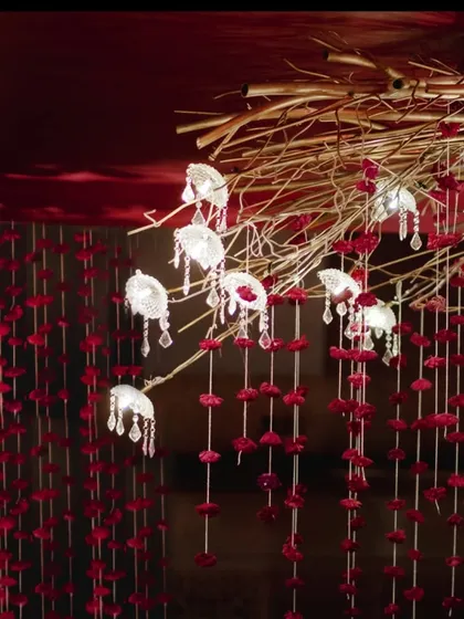 Custom-designed light fixtures featuring delicate glass lamps and crystal droplets hang from golden branches. These elements, combined with red floral strings, created a magical and mesmerizing ambiance over the mandap.