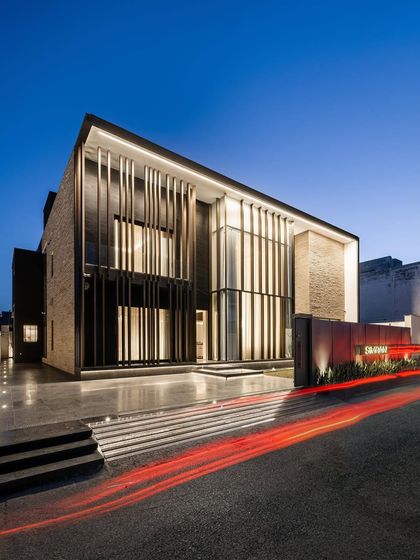 A view of the Silhouette home at dusk, where the architectural lighting highlights the dramatic vertical screens and the warmth of the interior spaces. The design creates a beacon of modernism in its neighborhood.