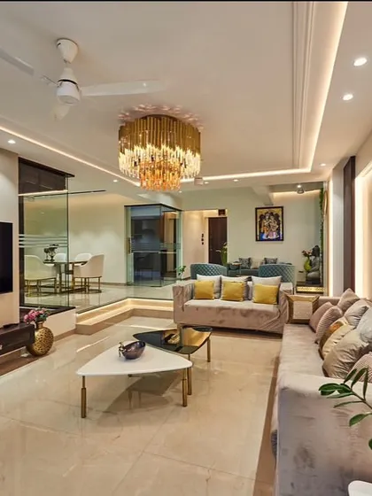 This living room design features a split-level layout, creating distinct zones for seating and passage. We used a grand chandelier and continuous profile lighting to unify the space, while the glass partition maintains a visual connection to the dining area.