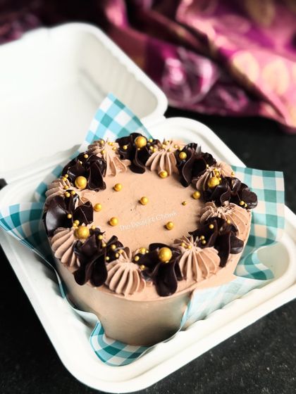 A simple and elegant chocolate bento cake with delicate piping and gold sprinkles.