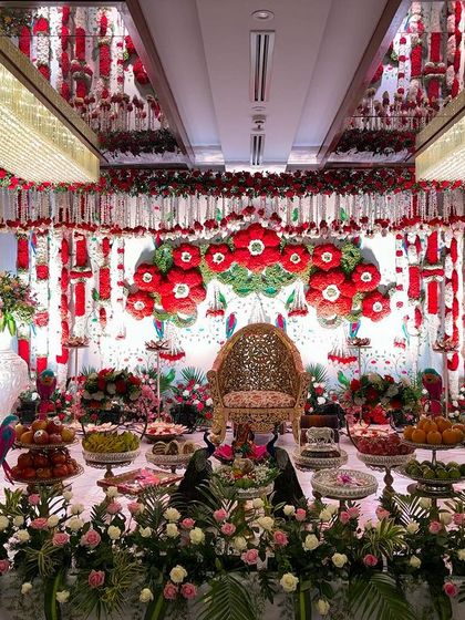 A vibrant stage dominated by red and white flowers, featuring large red floral medallions and hanging garlands. The mirrored ceiling reflects the colorful decor.
