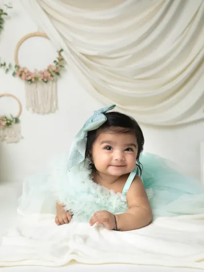 A beautiful, serene portrait of an infant lying on a soft white blanket. Her gentle smile and the dreamy mint green dress create a peaceful image.