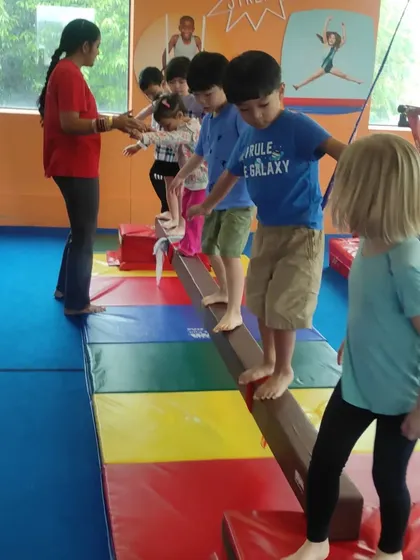 A coach guides a line of children across the balance beam, ensuring each child feels secure as they practice this important skill.