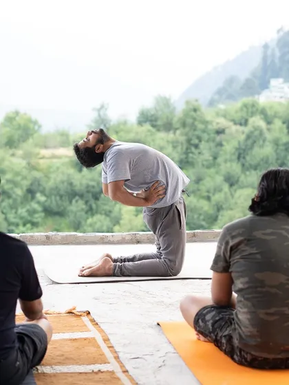 We integrate gentle physical practices like yoga to prepare the body for deep meditation. Here, a participant performs the Camel Pose (Ustrasana) during a mountain retreat, opening the heart and connecting with the expansive natural landscape around us.